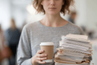 A youth carrying a stack of paperwork and a coffee cup