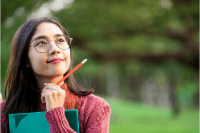 smiling young adult holding a book and pencil thinking about college plans 