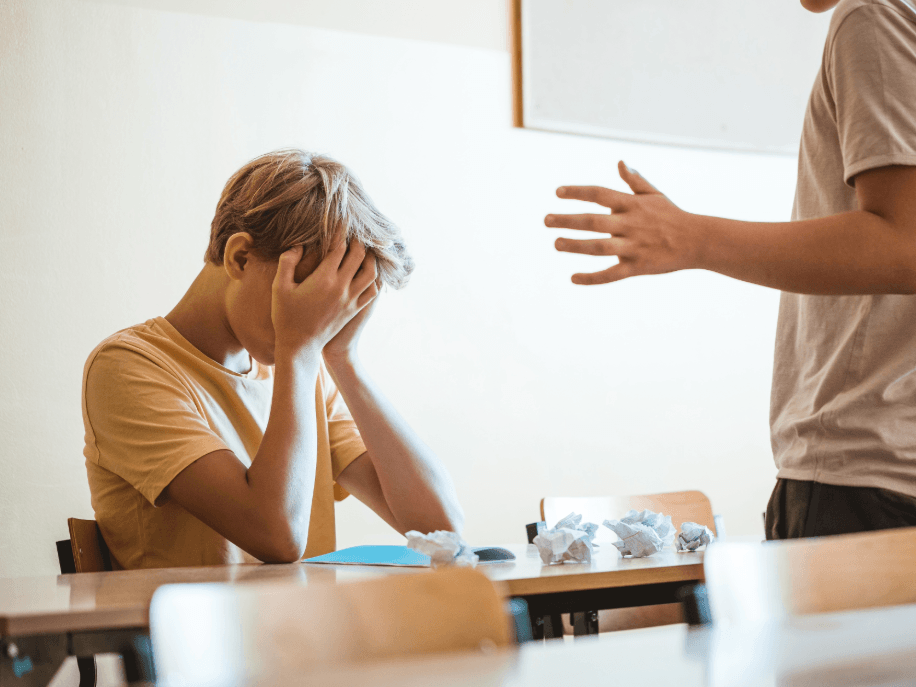 student with head in their hands, being talked to by their teacher at school